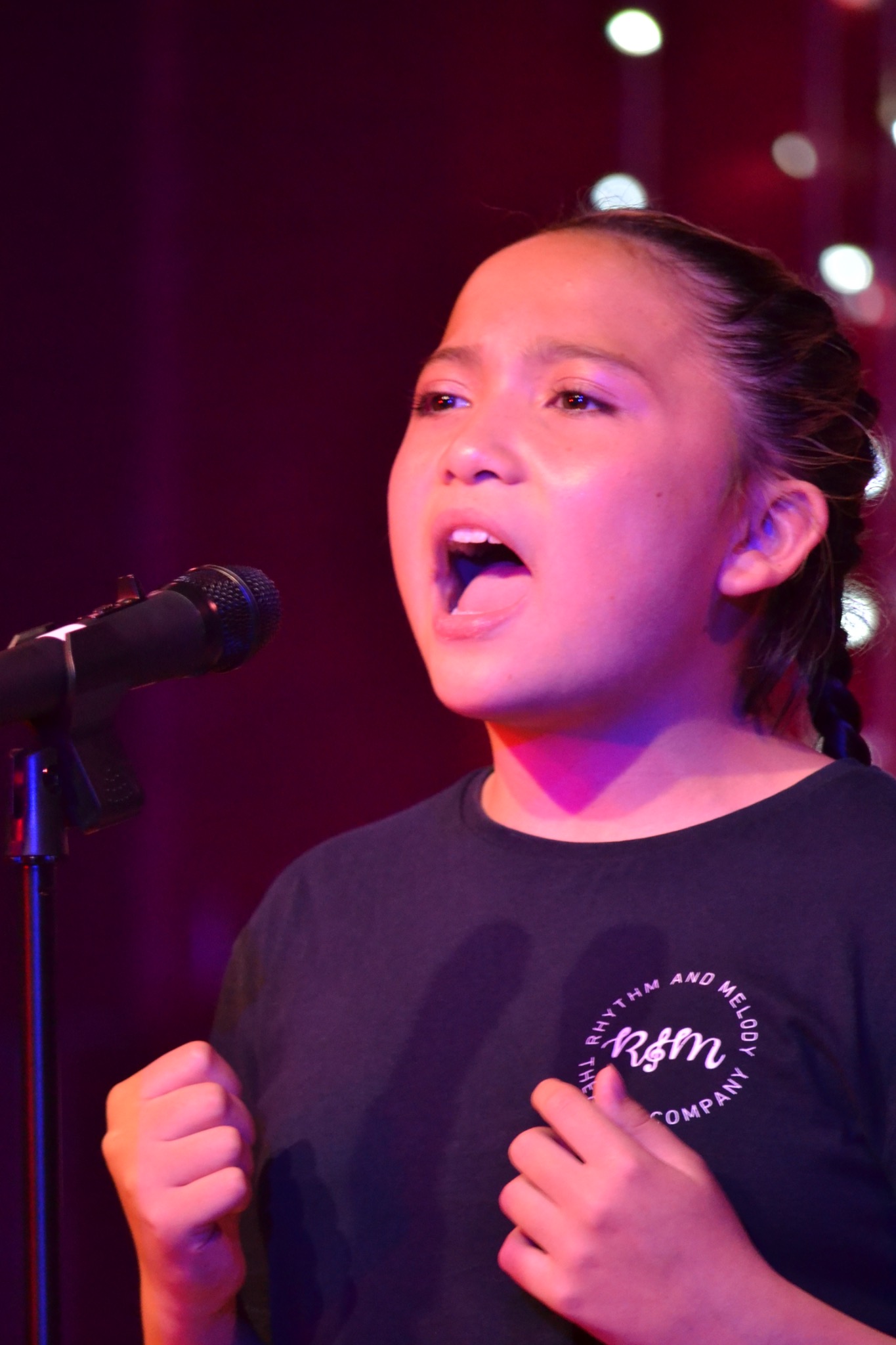 A performer sings into a microphone beneath colourful stage lights.